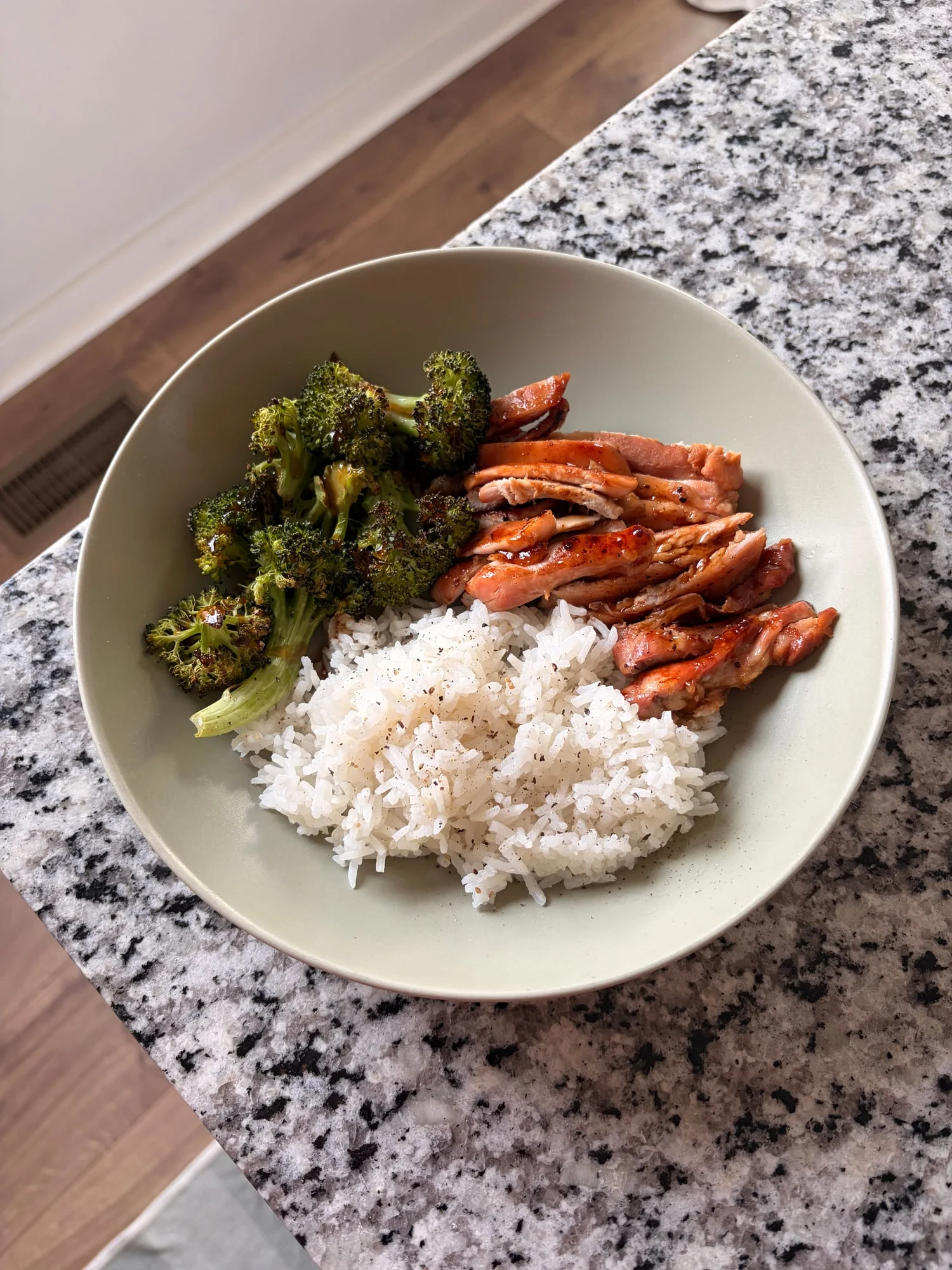 Sheet pan chicken teriyaki, sliced, with roasted broccoli and white rice in a sage bowl on a granite counter
